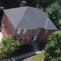 An aerial view of a large brick house with a black roof surrounded by trees.