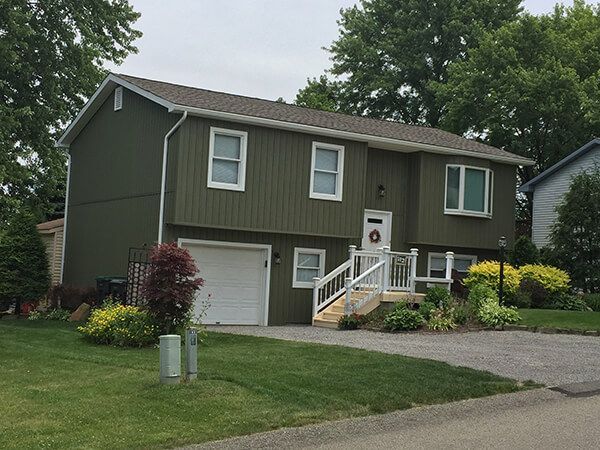 A green house with a white garage door and stairs