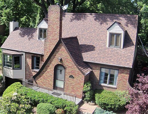 An aerial view of a brick house with a brown roof surrounded by trees.