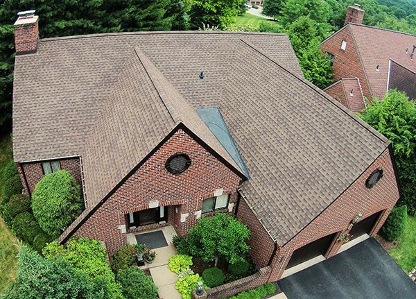 An aerial view of a large brick house with a brown roof surrounded by trees.