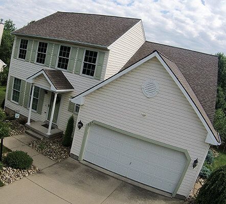 An aerial view of a white house with a brown roof and a white garage door.