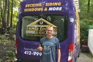 A man is standing in front of a purple van that says decking siding windows and more.