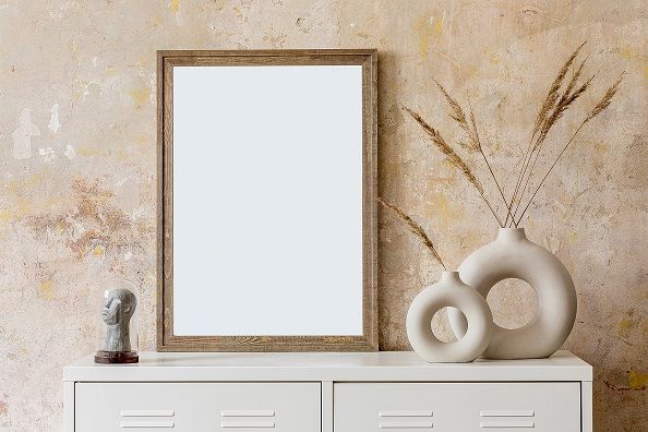 Wooden framed print, white dresser with vases and a bust sculpture against a textured beige wall.