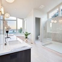 Modern bathroom with a glass shower, white countertops, and a window view.