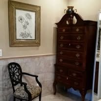 Wooden dresser, ornate chair, and framed artwork in a room with beige walls.