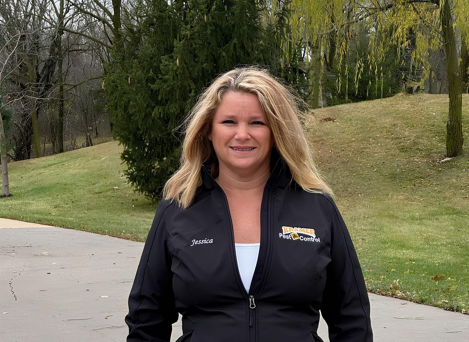 Woman in black jacket stands outside, smiling.