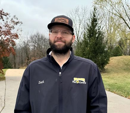 Man in black jacket and hat stands outdoors on a driveway.