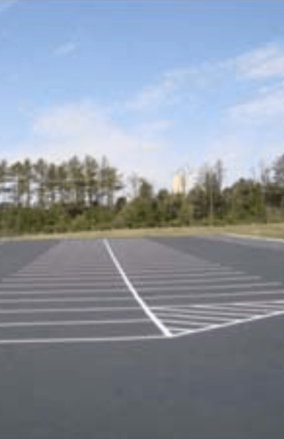 An empty parking lot with trees in the background on a sunny day.
