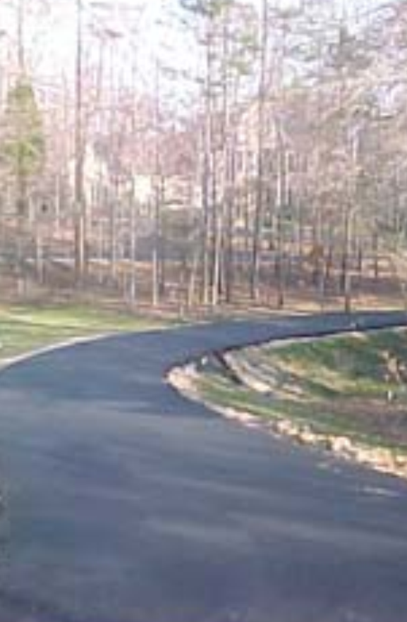 A car is driving down a curvy road in the woods.