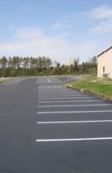 A parking lot with a house in the background and a blue sky.