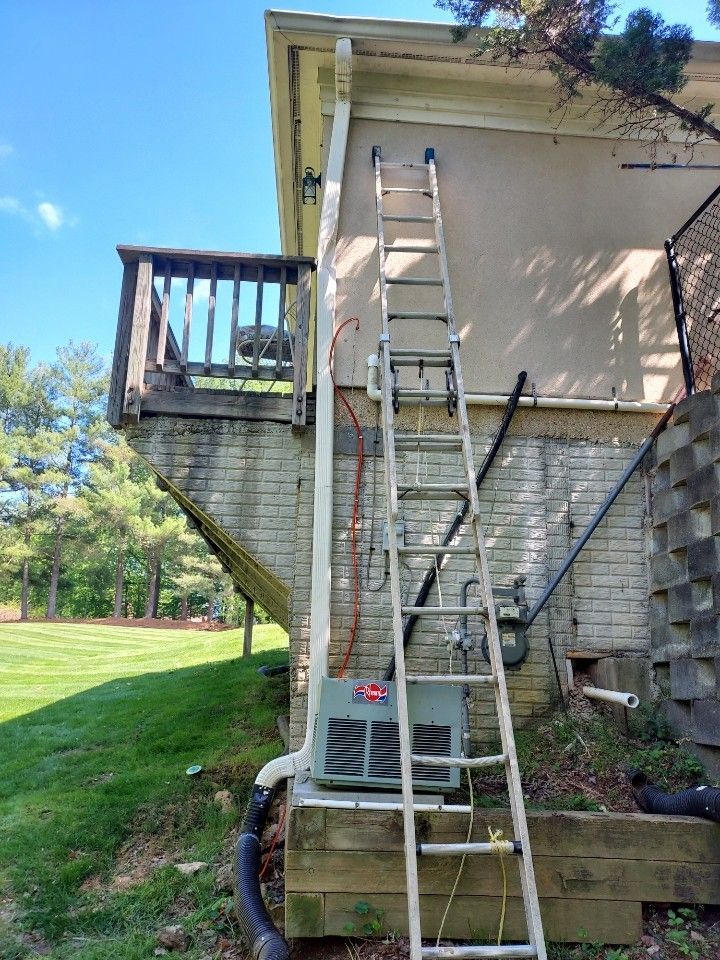 Ladder leaning against a house beside a deck and air conditioner outside on a sunny day