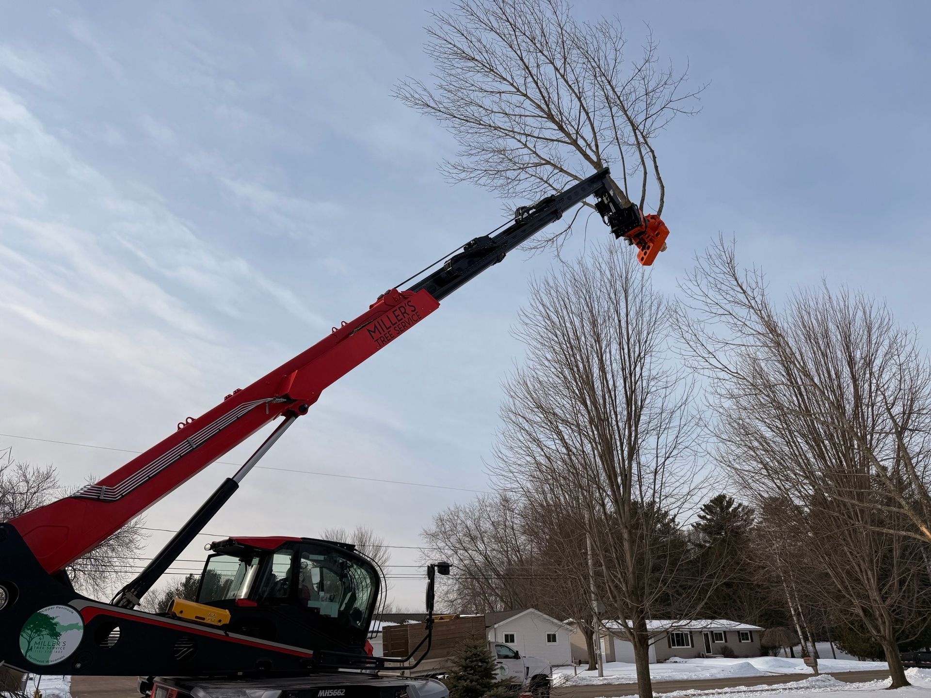 Red crane lifting tree branches in a snowy yard under a cloudy sky