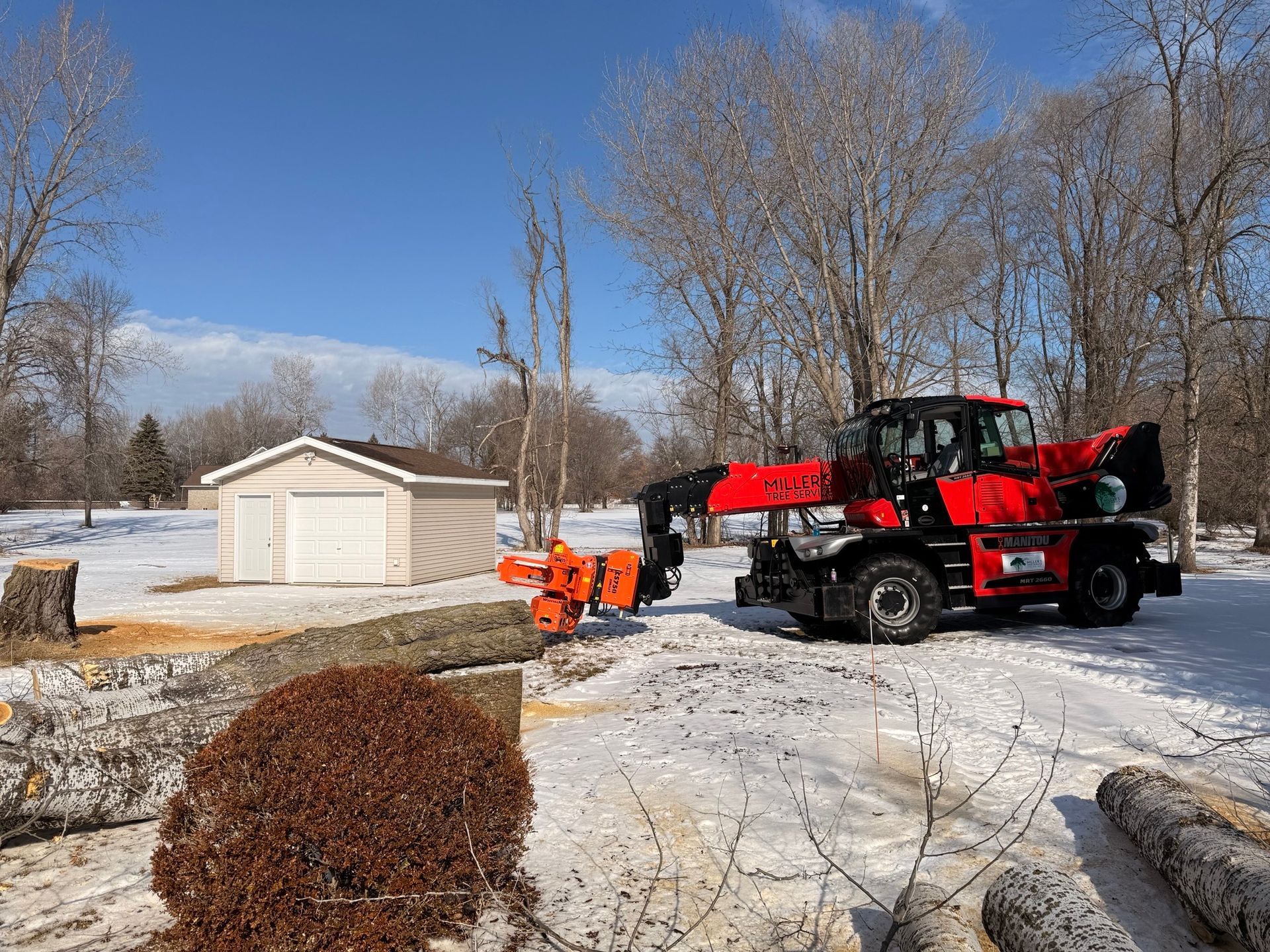 Red tractor clearing snow in a snowy yard beside a white shed and bare trees