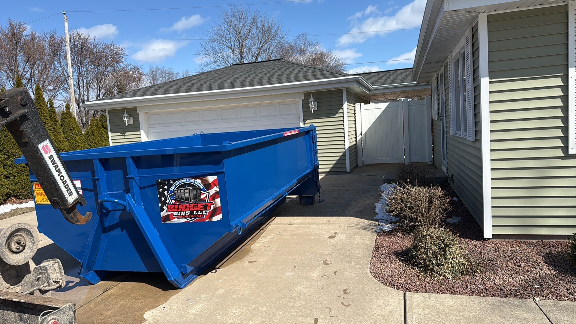 Blue dumpster parked on the garage of a house.