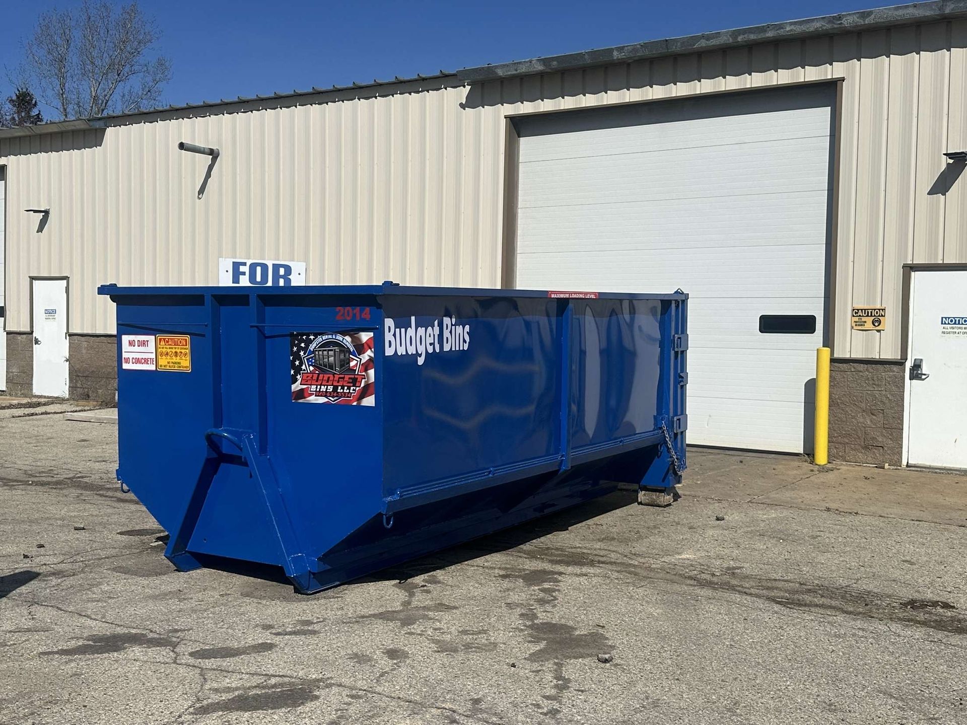A large blue dumpster in the back of a white building.