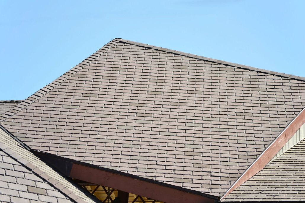 A close-up of a brown asphalt shingle roof against a clear blue sky.