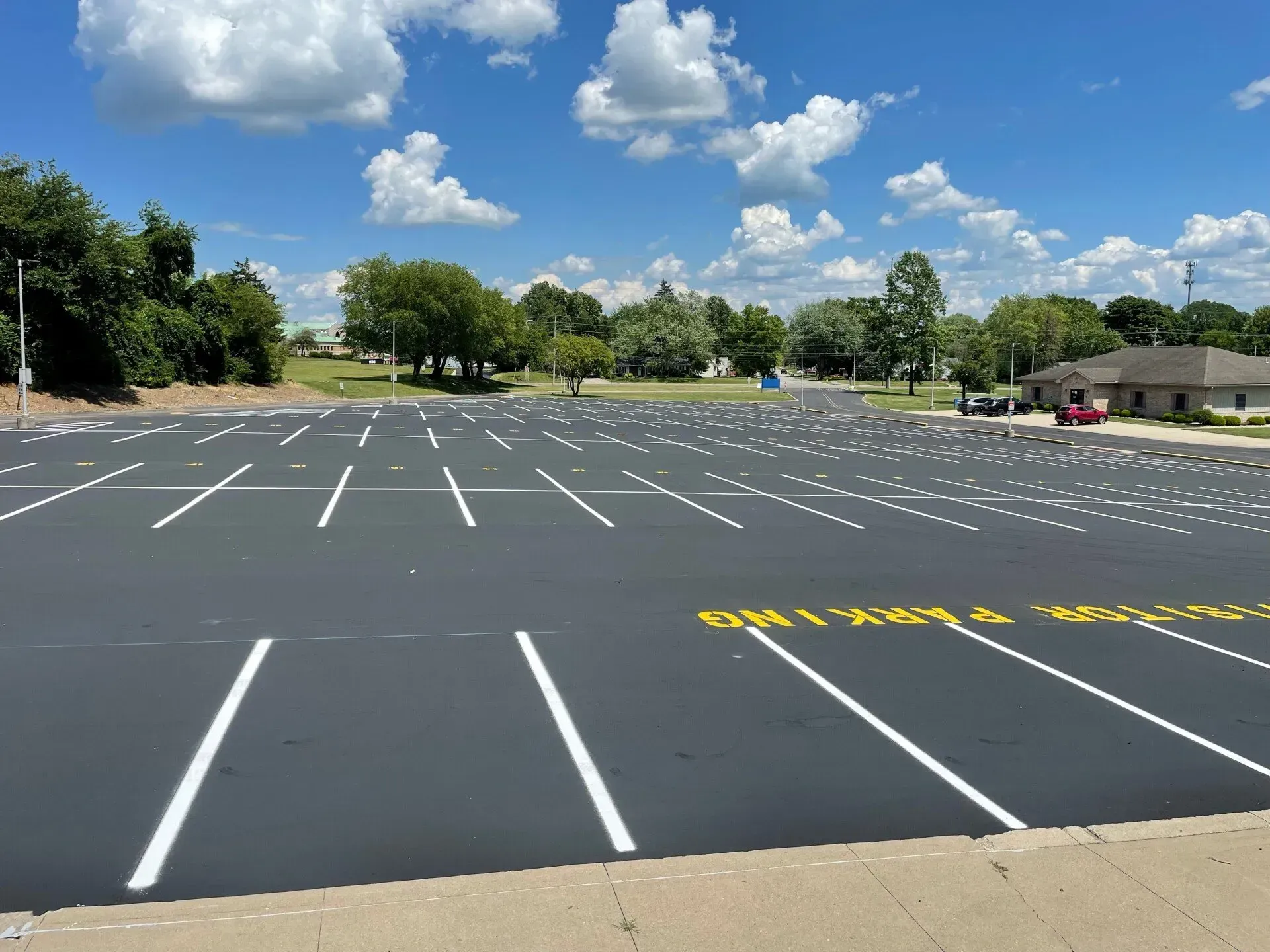 A newly paved, empty parking lot with white painted lines under a bright blue sky with scattered clouds.