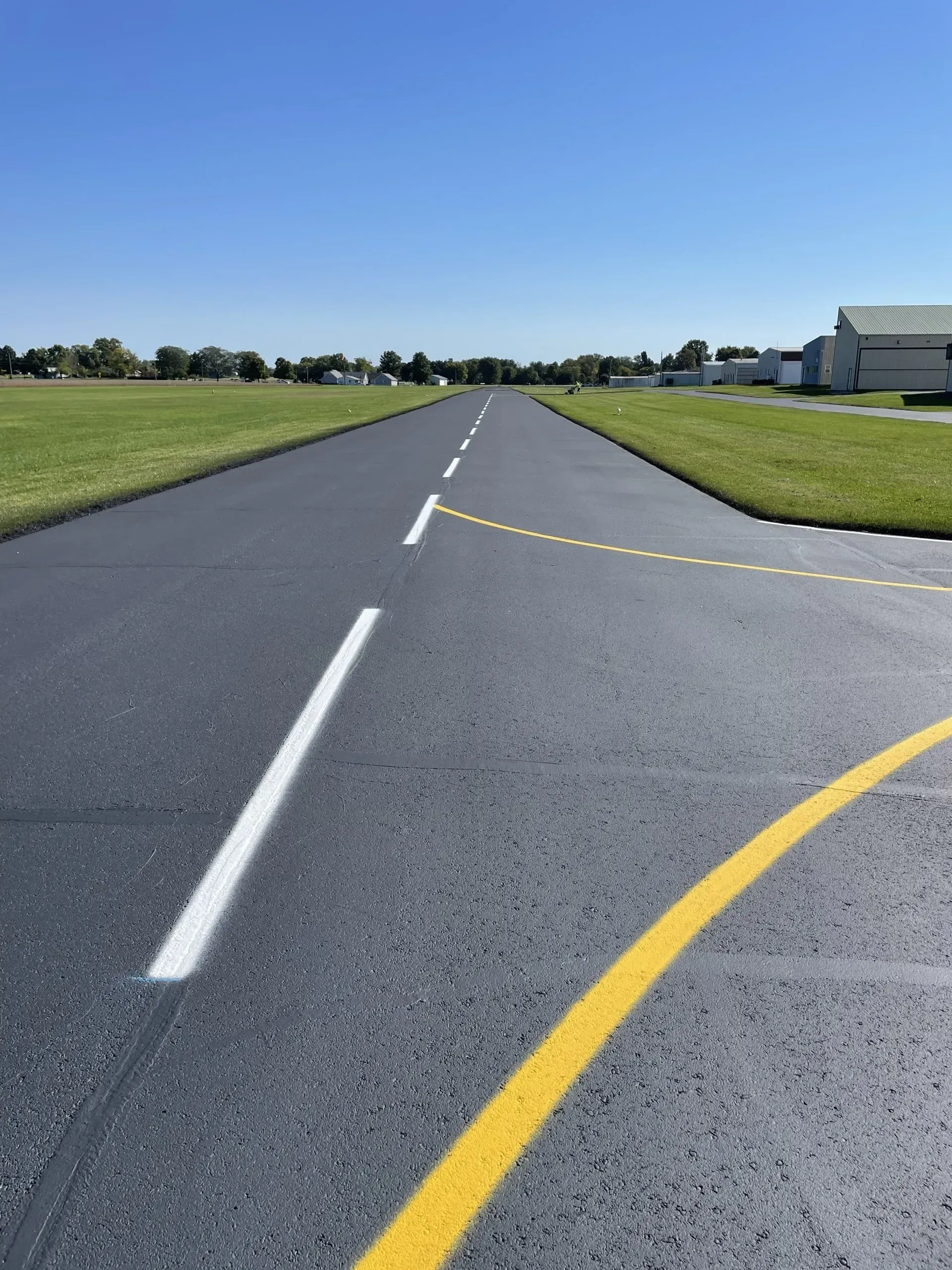 Paved path leading into the distance with white dashed lines and a yellow painted curve against a clear blue sky.