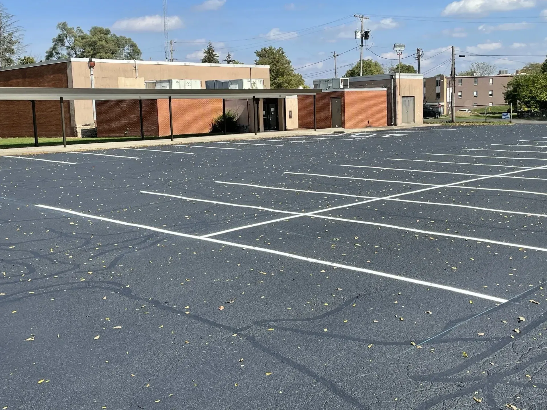 A parking lot with marked spaces, some scattered leaves, and a low brick building under a blue sky.