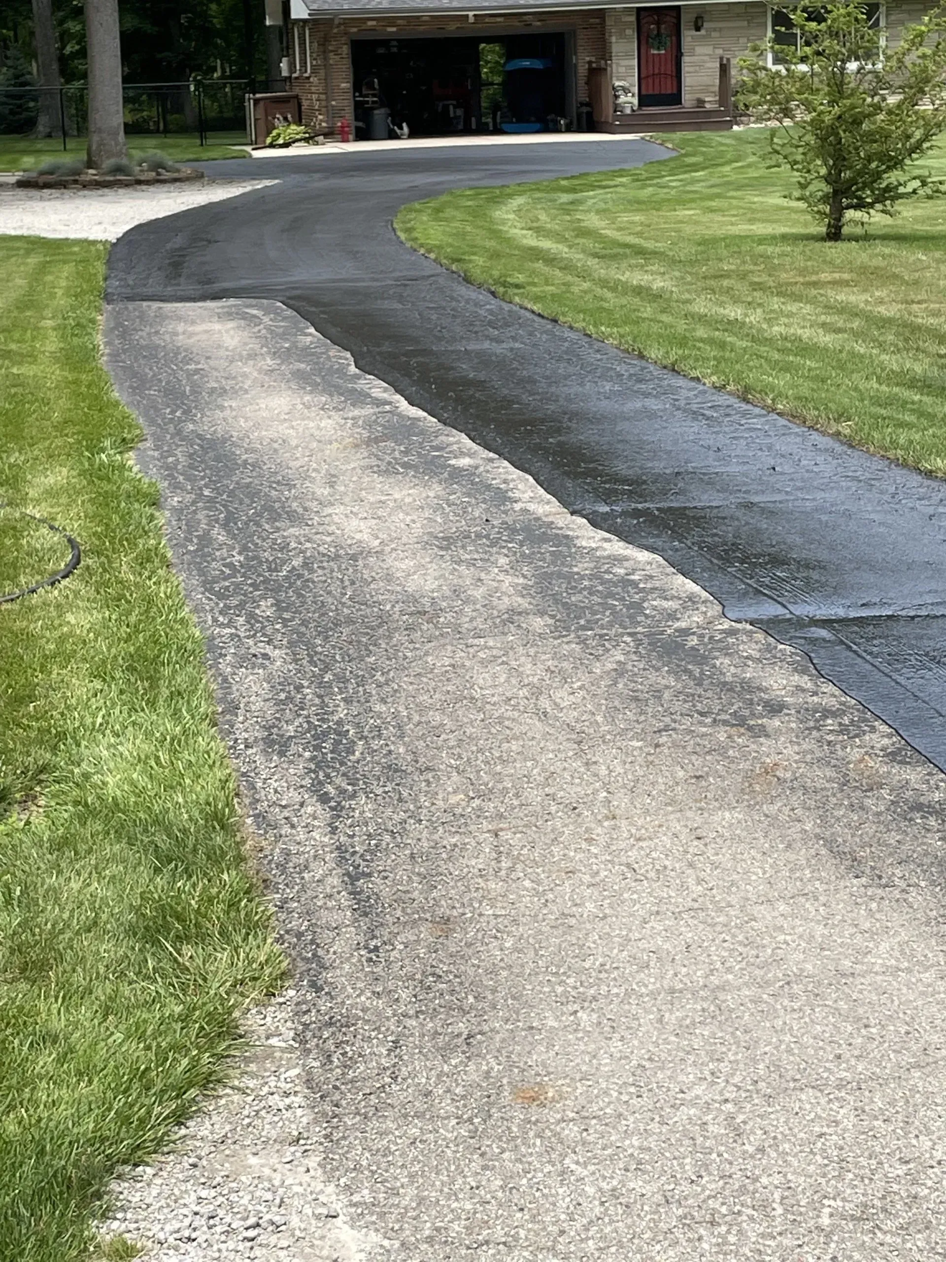A residential driveway featuring a section of fresh, dark asphalt alongside a section of older, weathered grey gravel.