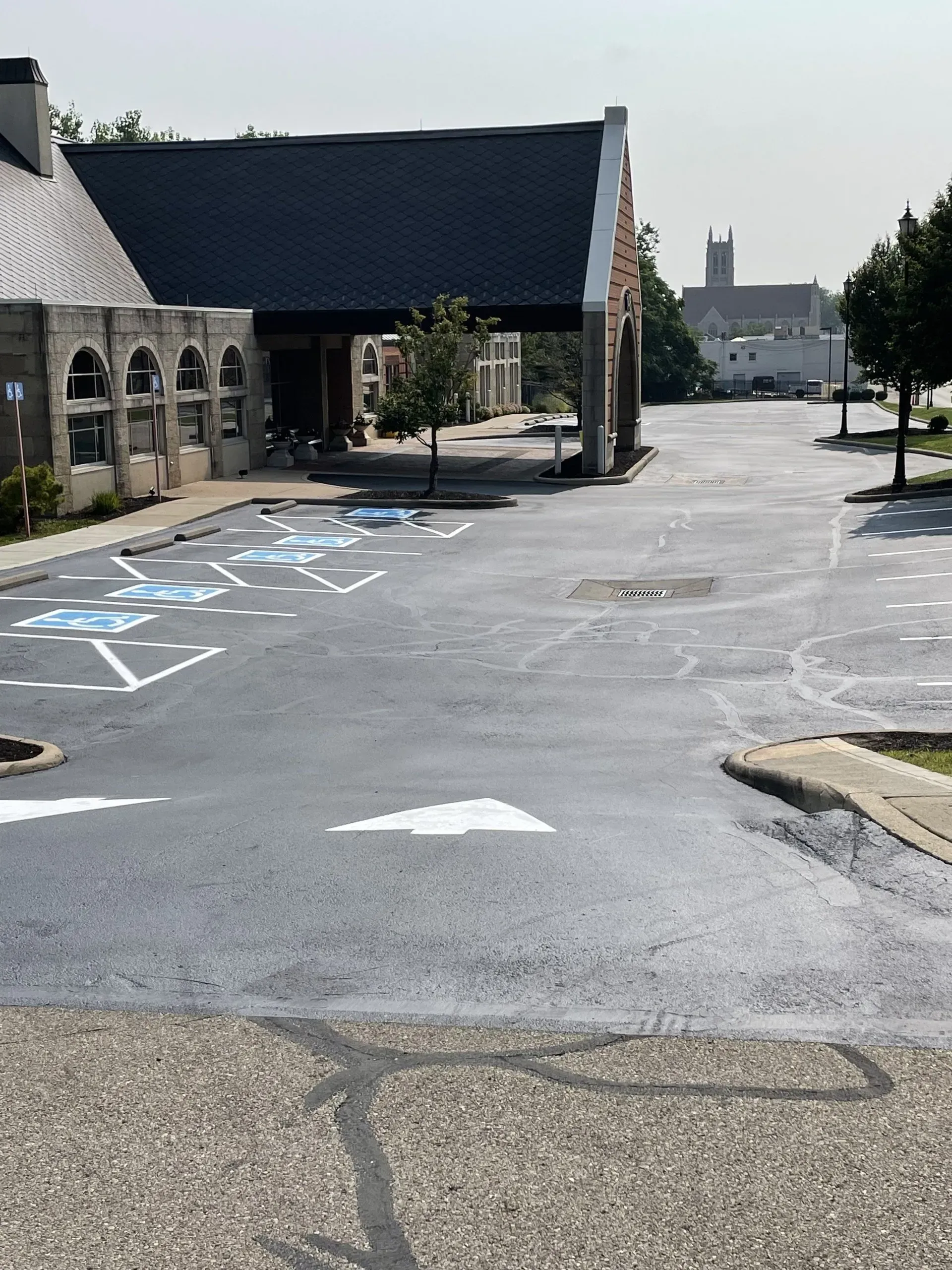 A paved parking lot with white directional arrows leads toward a stone building with a covered entrance.