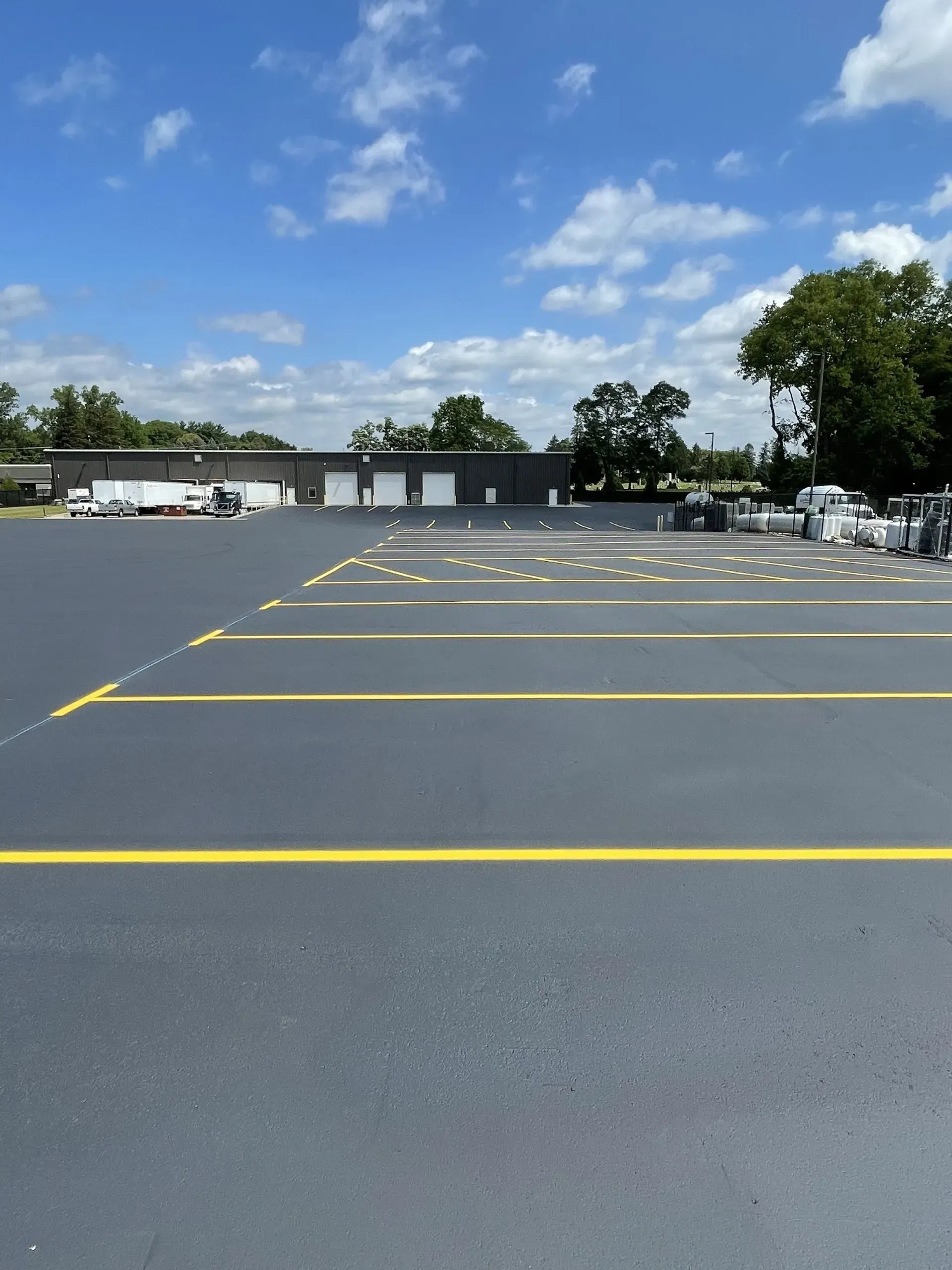 Freshly paved parking lot with bright yellow painted lines under a blue sky with scattered clouds.