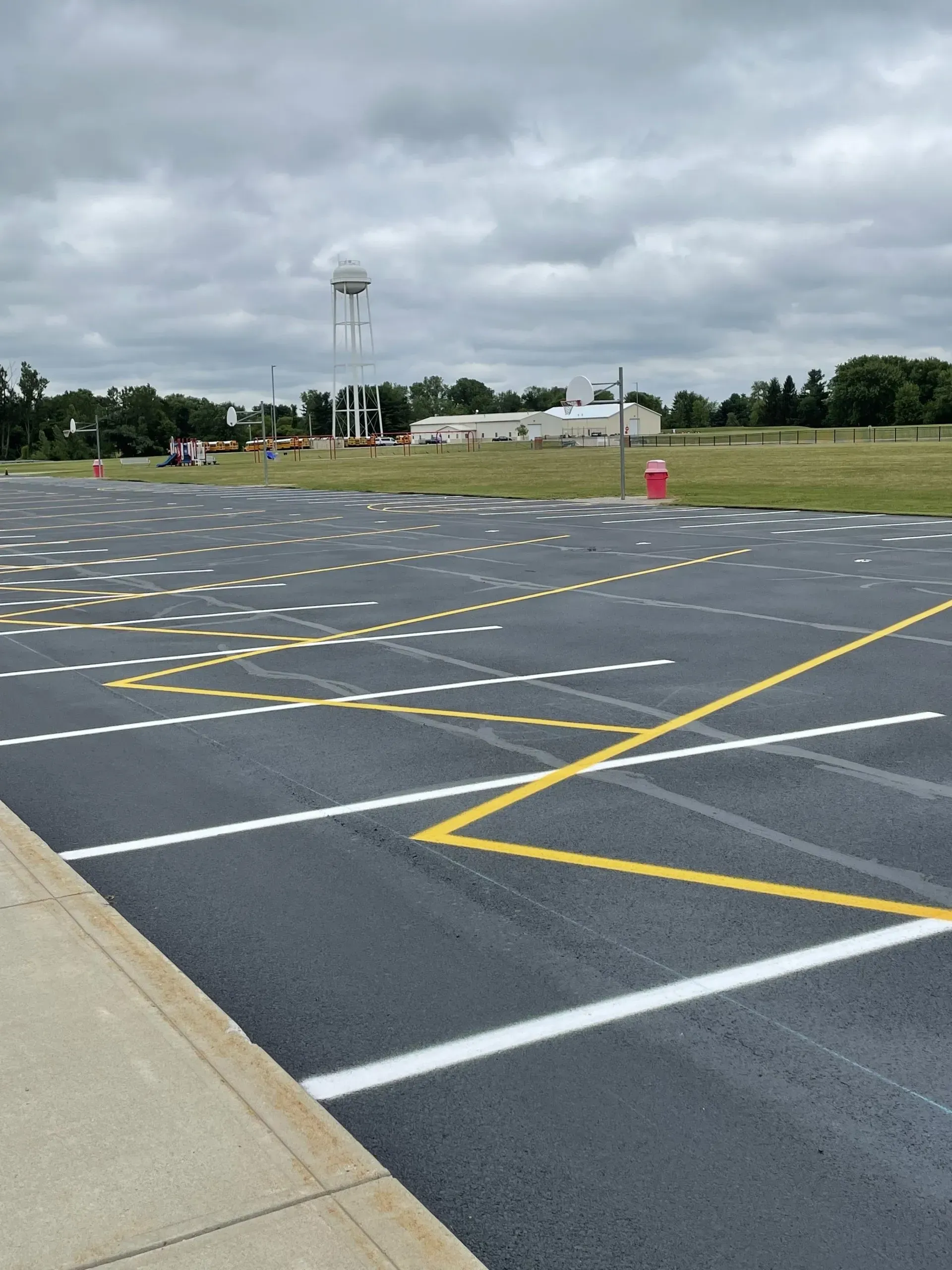 A paved parking lot with white marked spaces, a yellow zigzag line, and a distant water tower under a cloudy sky.