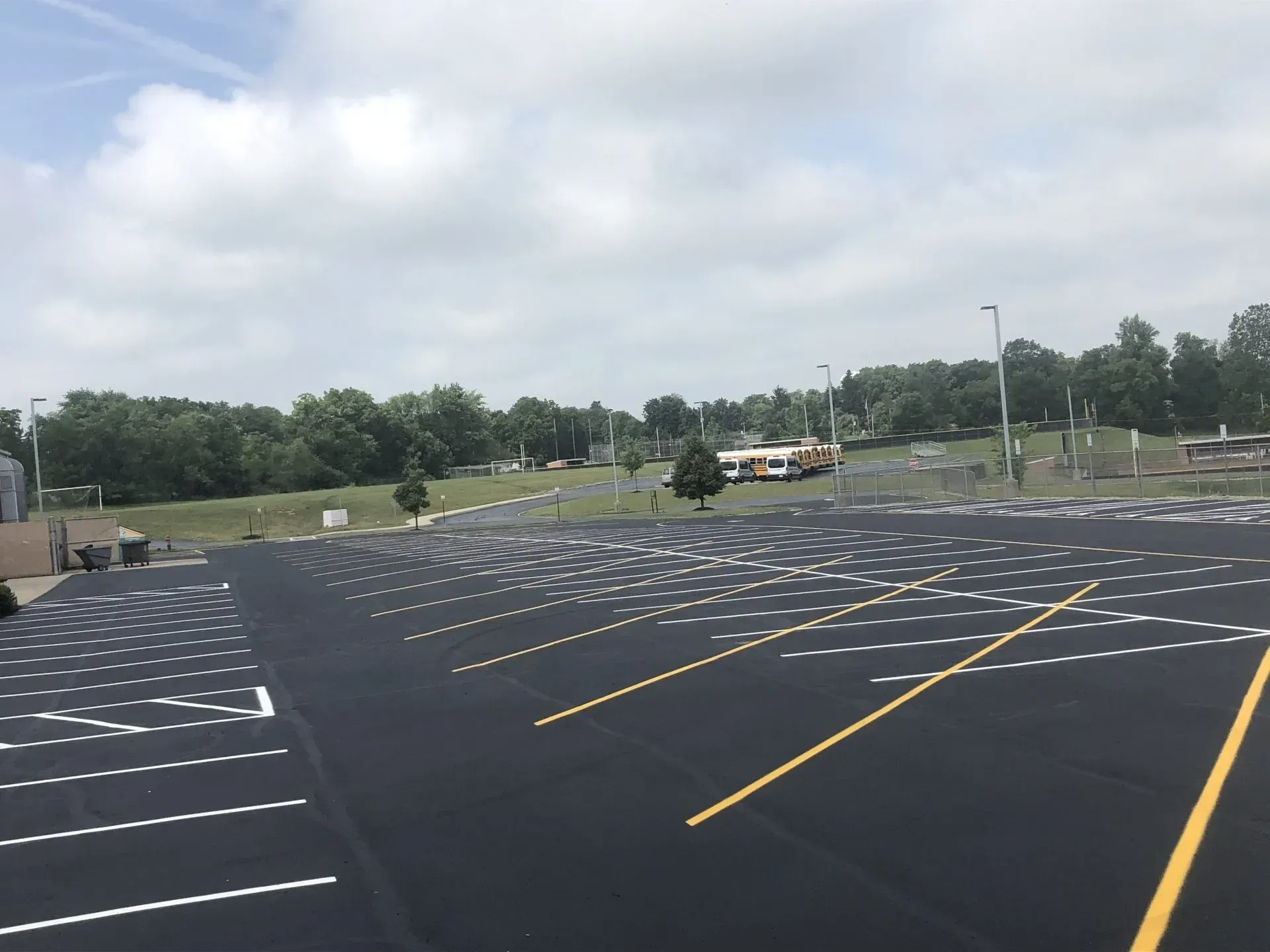 A parking lot with freshly paved black asphalt, marked by white parking lines and yellow directional lane dividers.