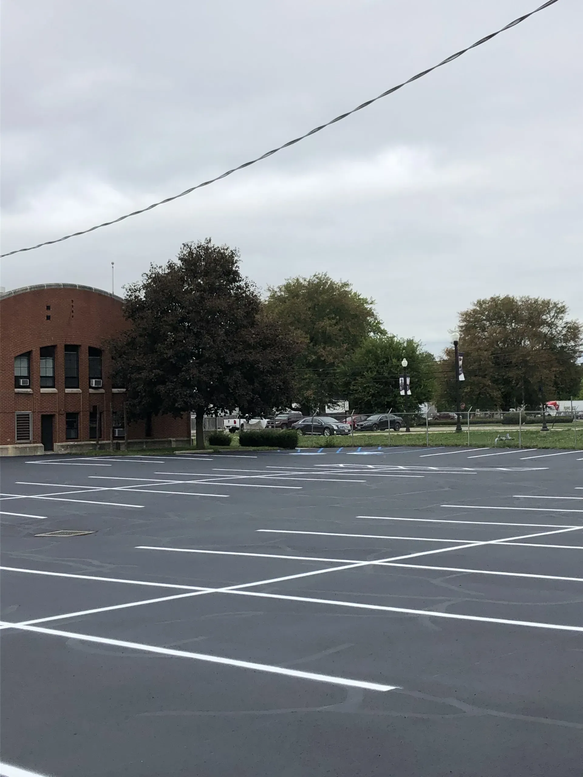 A brick building sits next to an empty parking lot featuring freshly painted white parking space lines on asphalt.