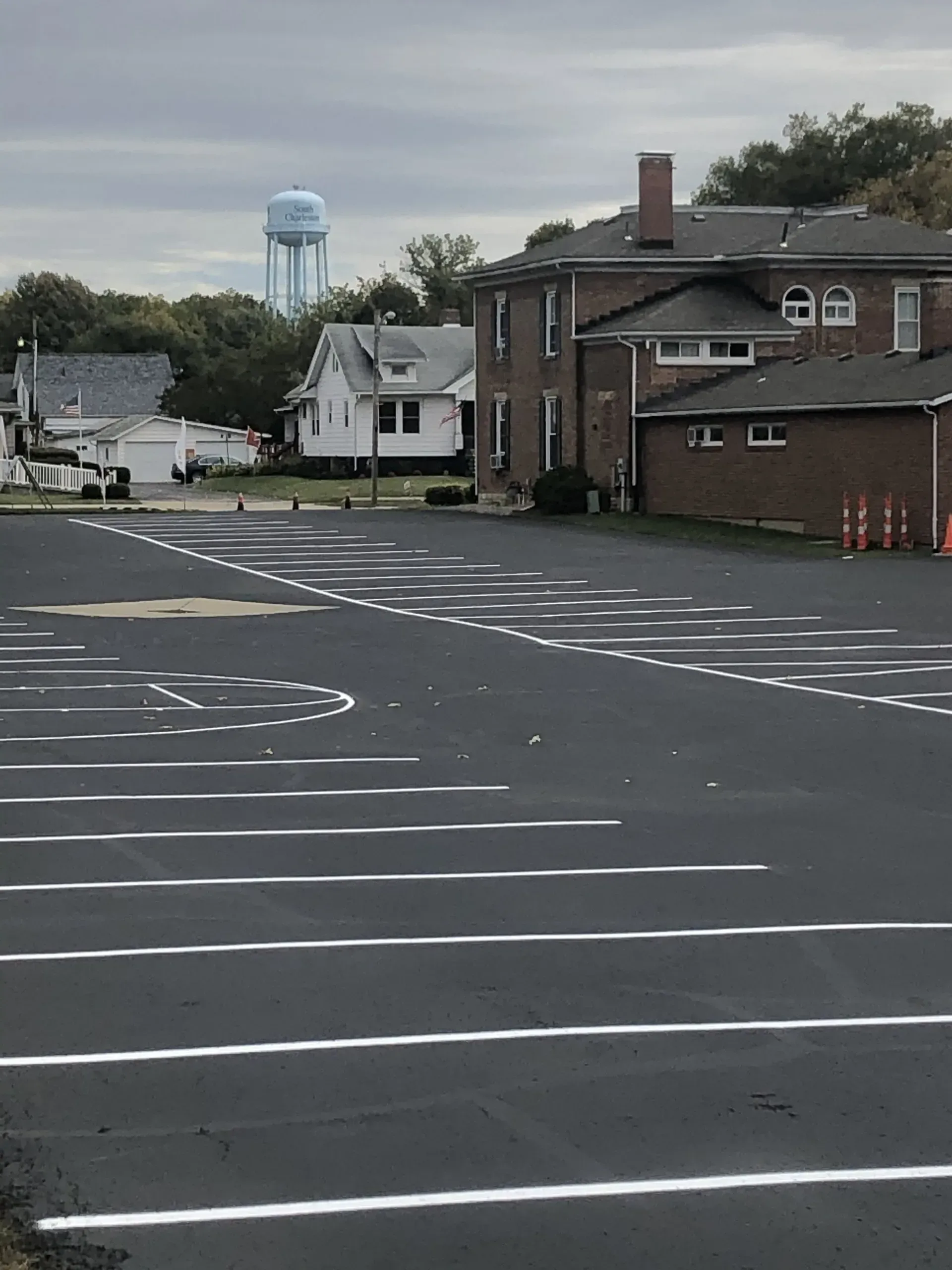 An asphalt parking lot with fresh white painted parking lines and markings, a brick house, and a blue water tower nearby.