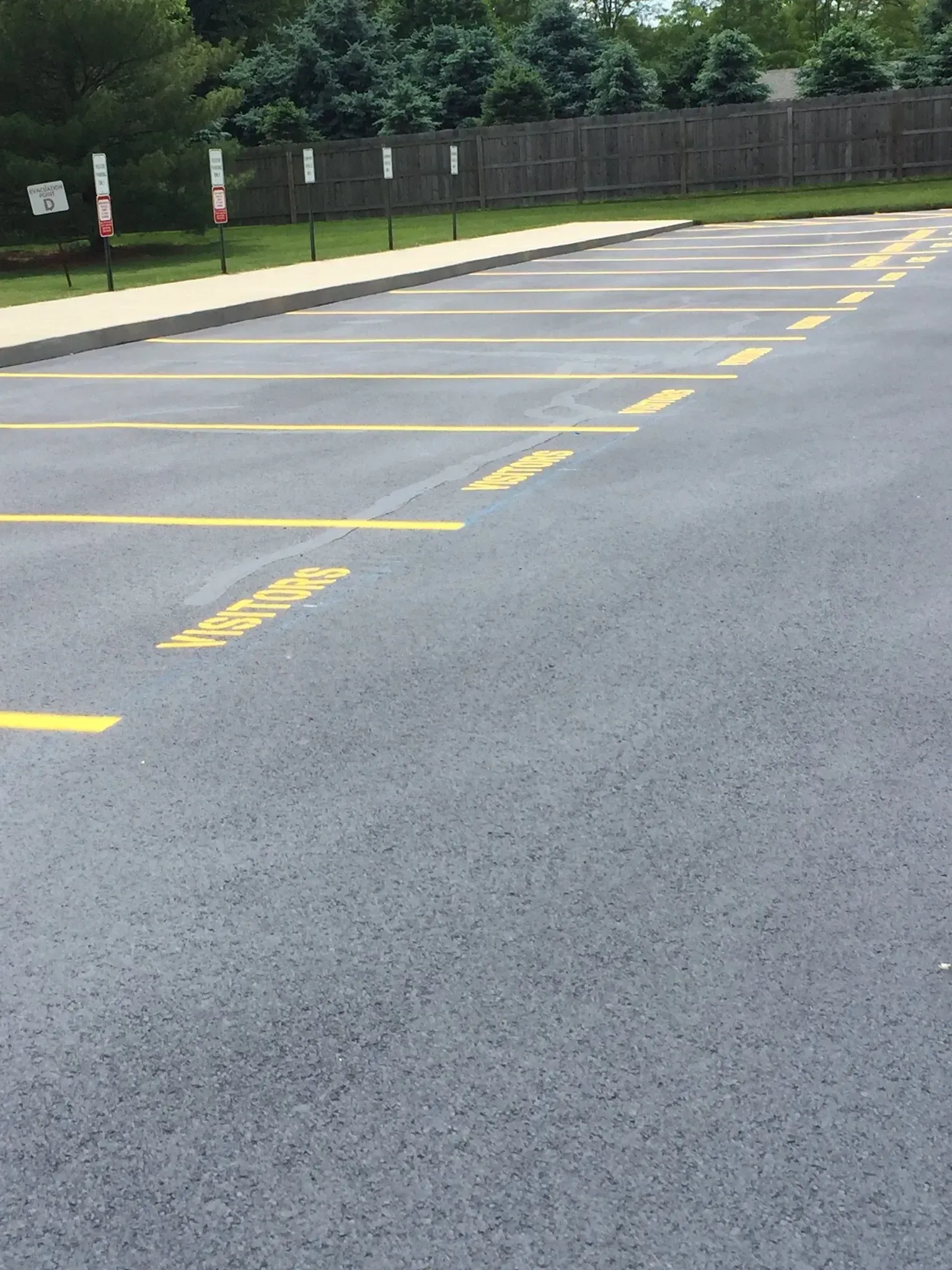 An empty parking lot with yellow-painted parking space dividers and painted text on the asphalt, near a wooden fence.