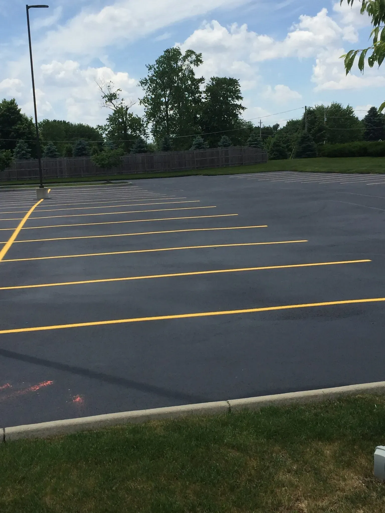 A paved parking lot with yellow-painted parking space lines under a partly cloudy sky.