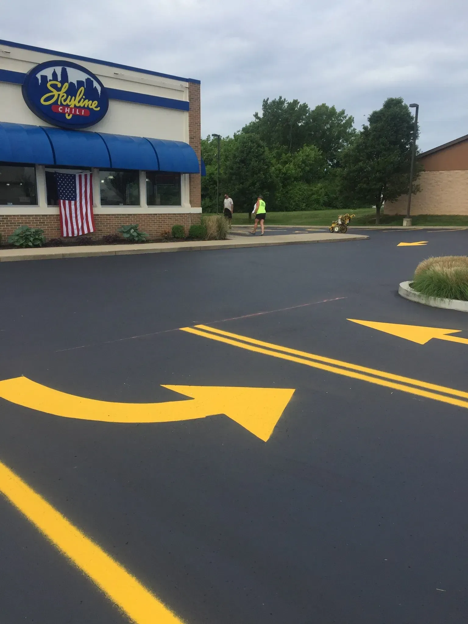 Parking lot with yellow directional arrows, leading toward a Skyline Chili restaurant with an American flag displayed.