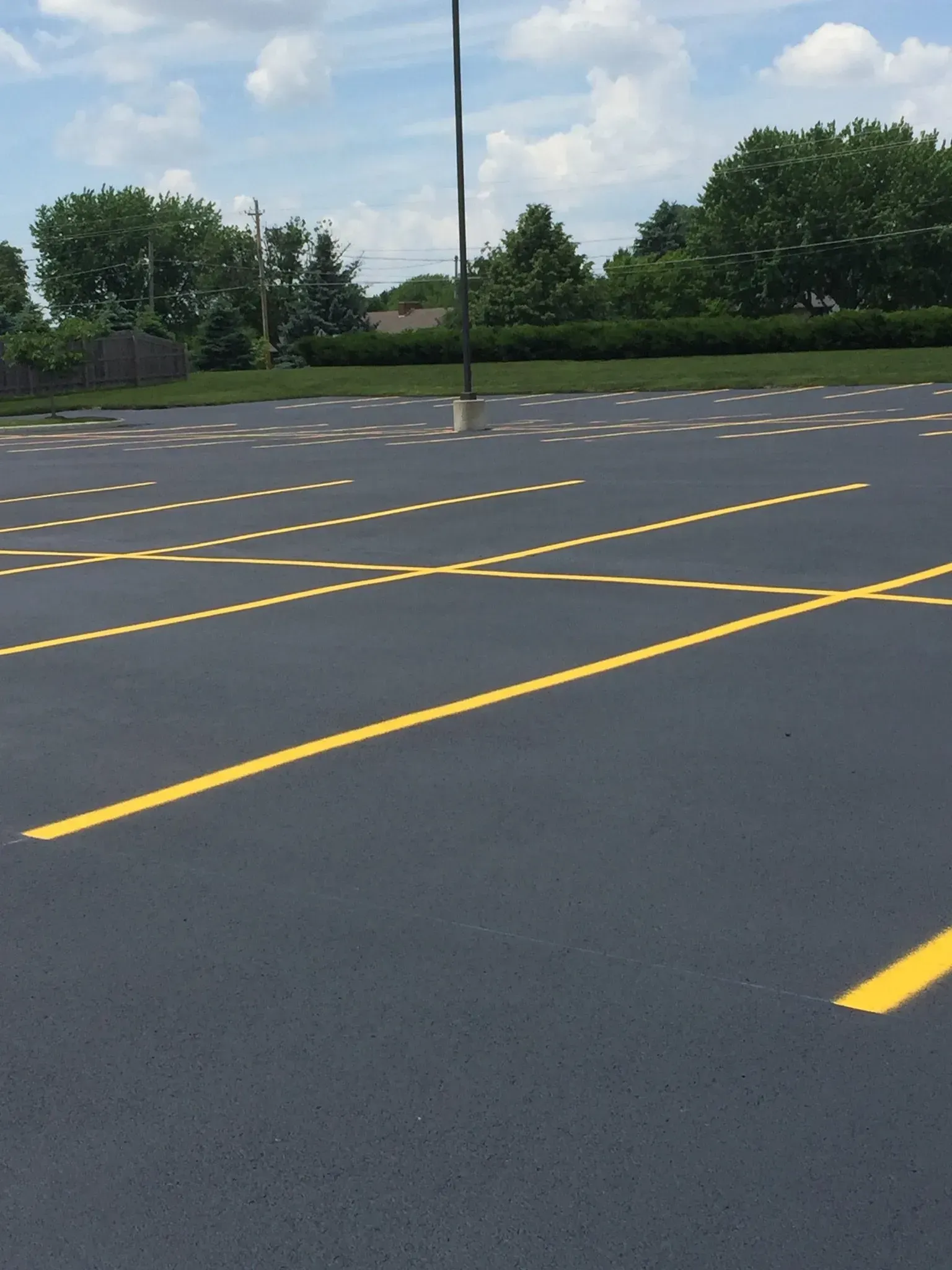 Empty asphalt parking lot with bright yellow painted diagonal parking space lines under a blue sky with clouds.