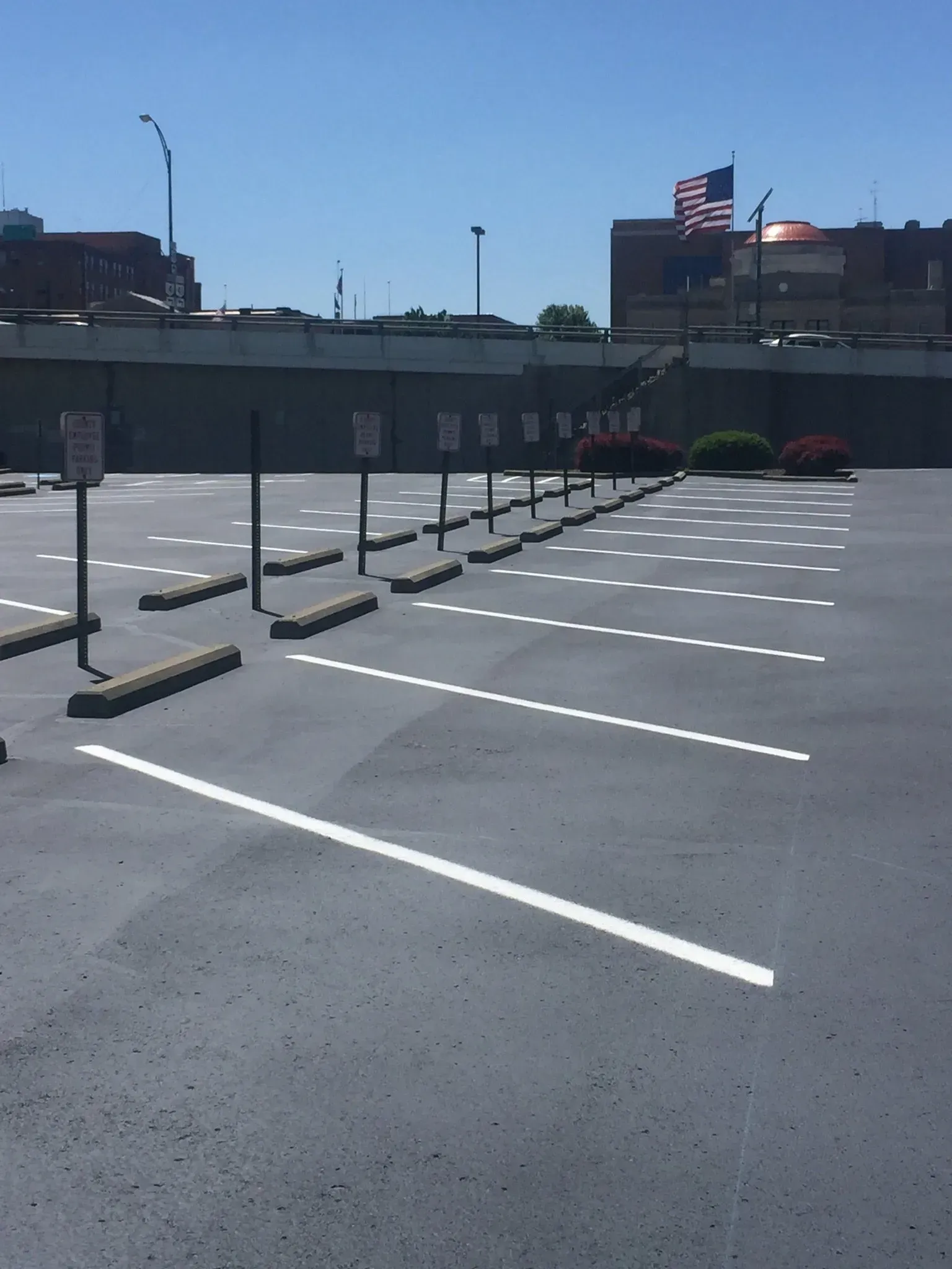 An empty parking lot with white painted spaces, concrete bumpers, and signage on a sunny day.