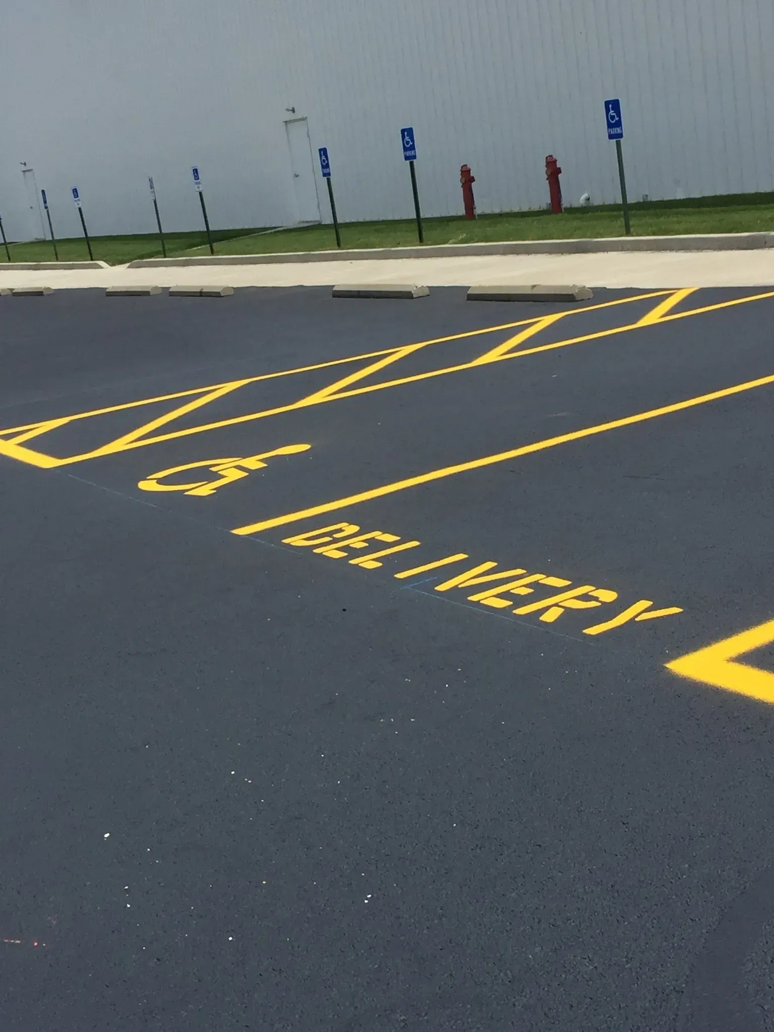 A paved parking lot with yellow-painted handicap and delivery zone markings, featuring blue accessibility signs.