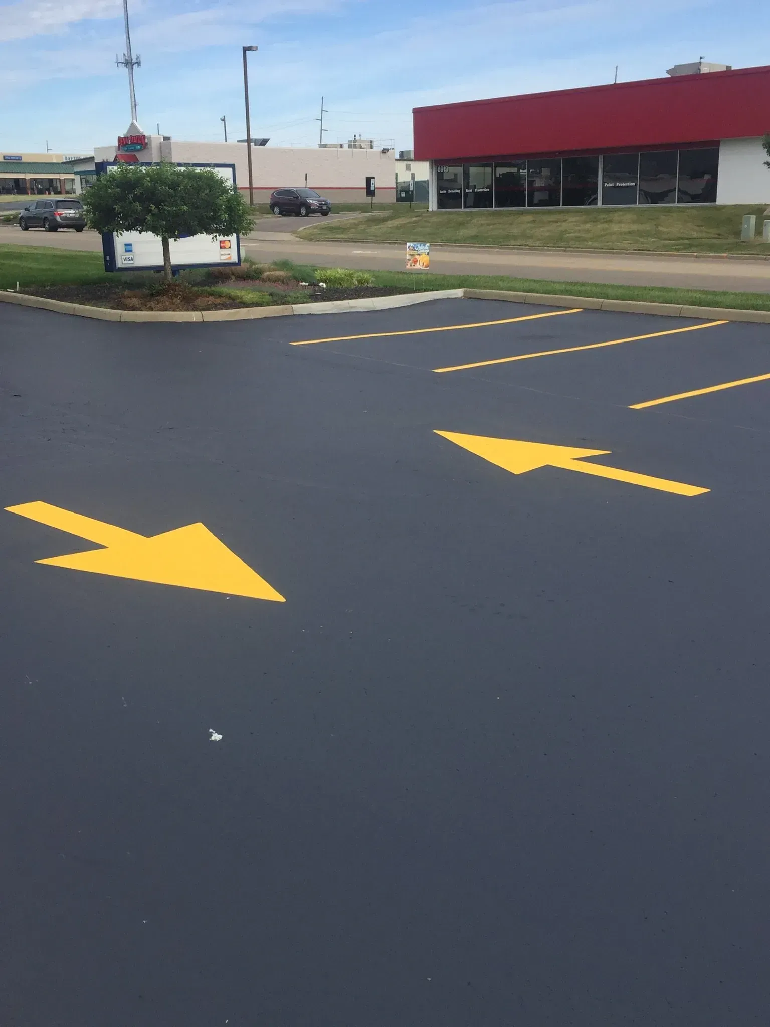 An asphalt parking lot with bright yellow painted directional arrows and dashed lane markings.