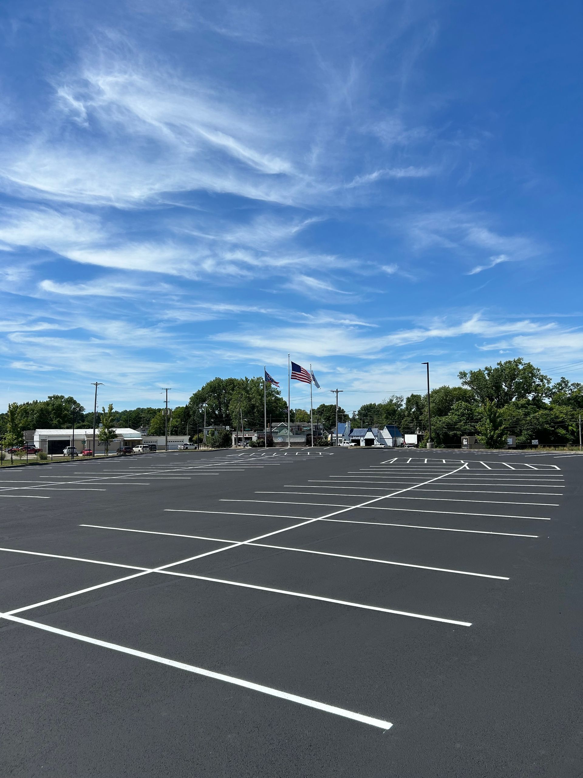 A newly paved parking lot with freshly painted white stall lines under a bright blue sky with wispy clouds.