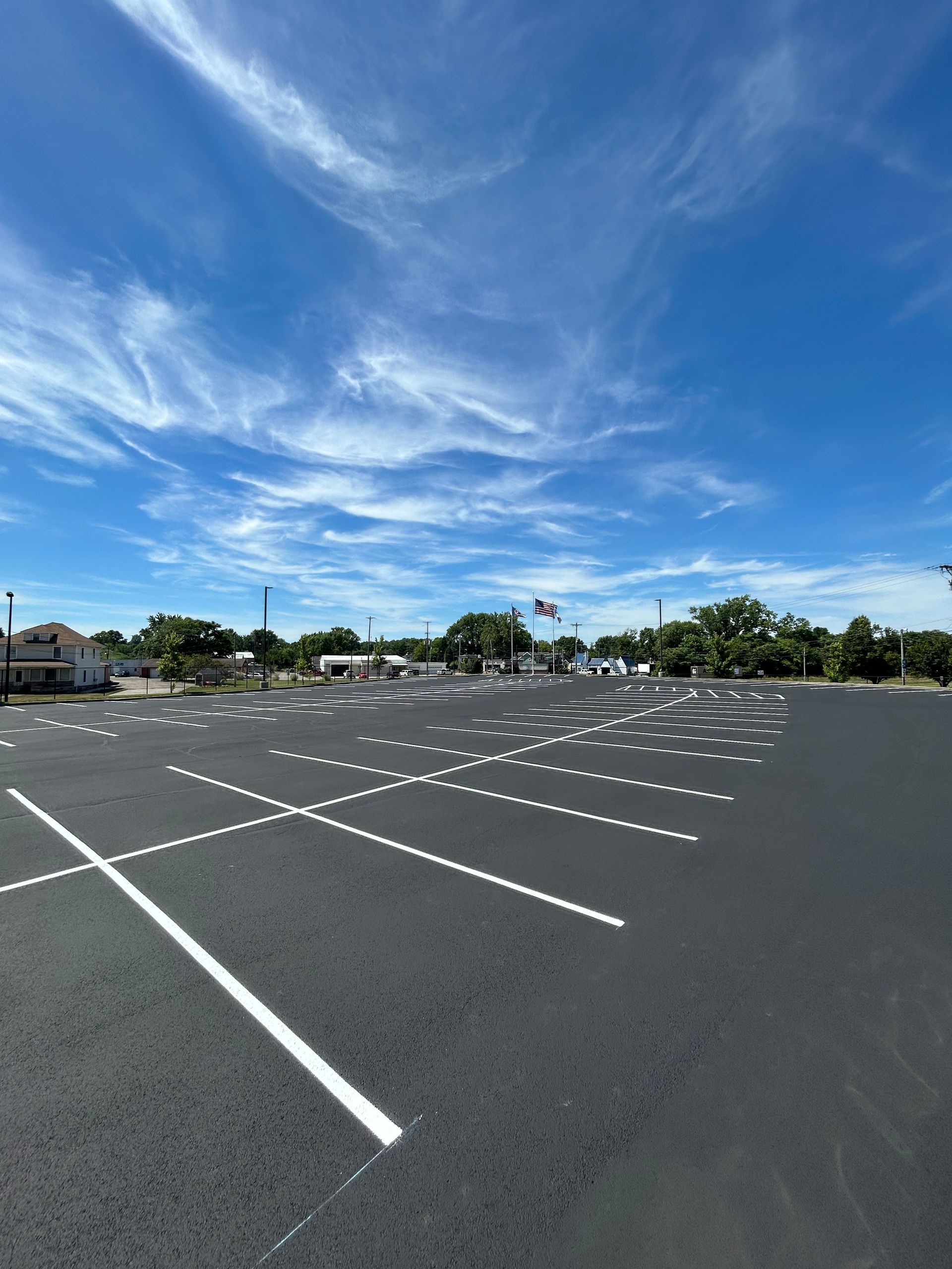A wide-angle view of a newly paved, empty parking lot under a bright blue sky with wispy clouds.