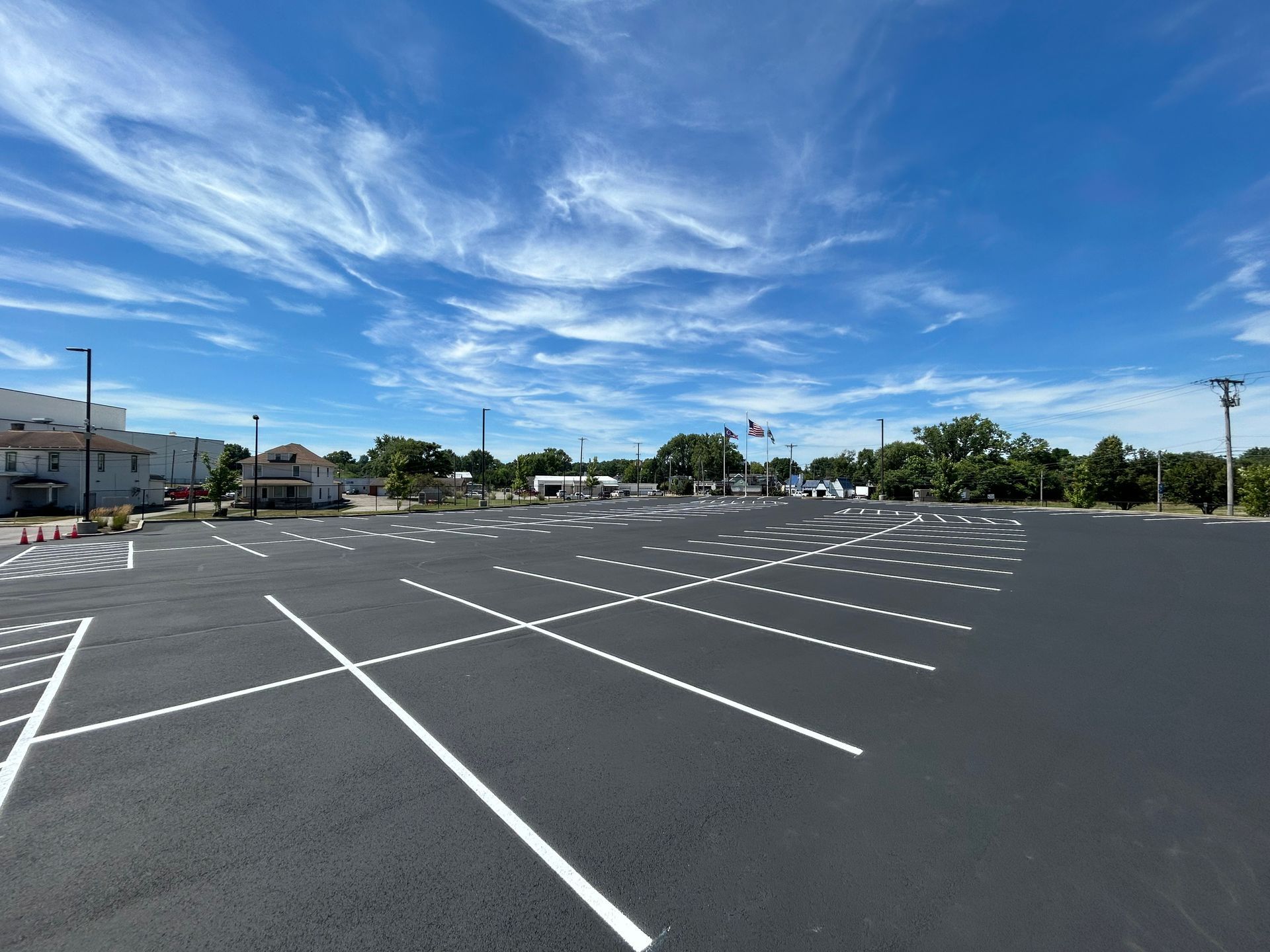 A freshly paved, empty asphalt parking lot with bright white painted lines under a vibrant blue sky with wispy clouds.