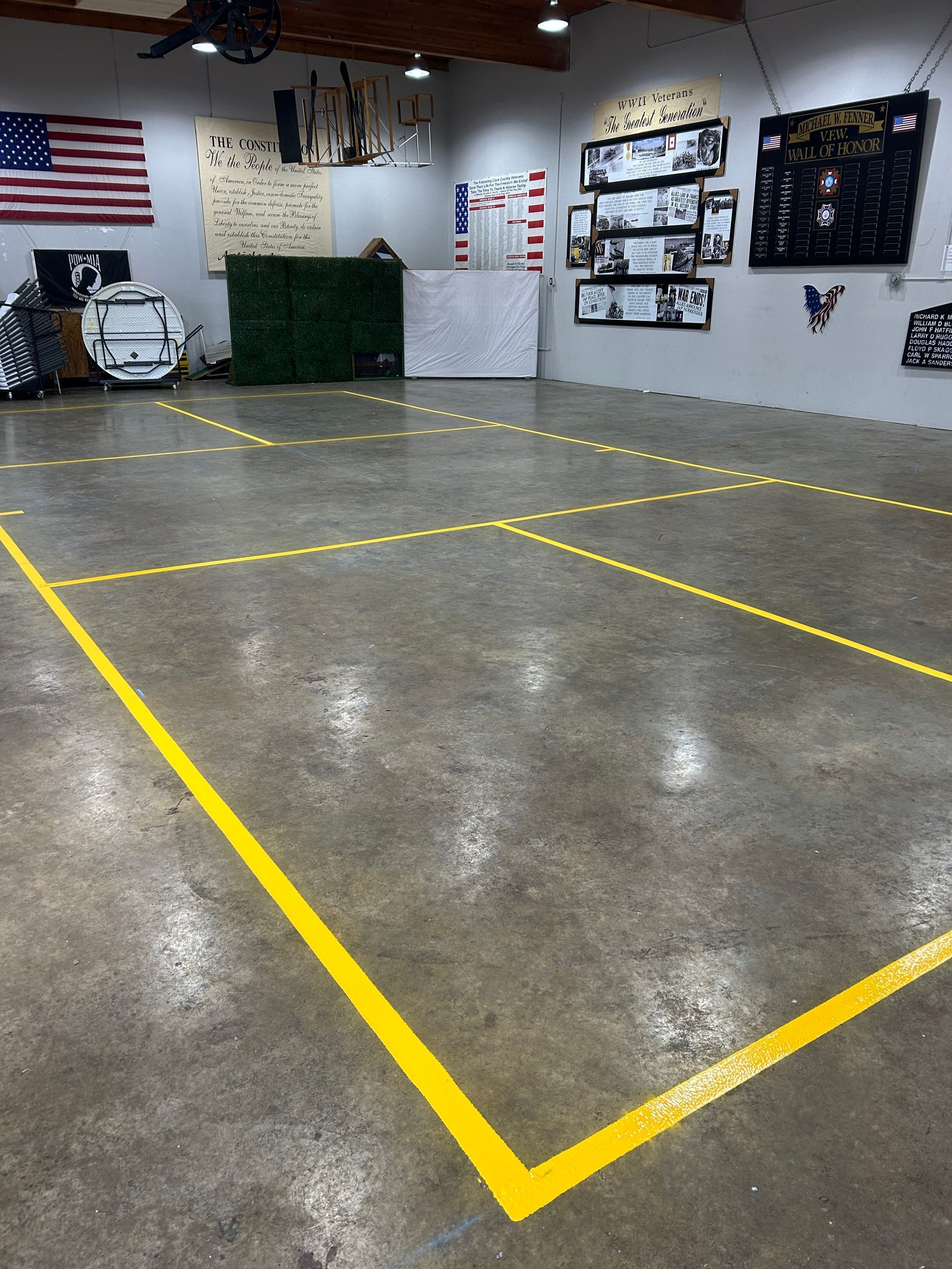 An indoor concrete space with bright yellow painted lines marking rectangular floor zones, American flag, and wall art.