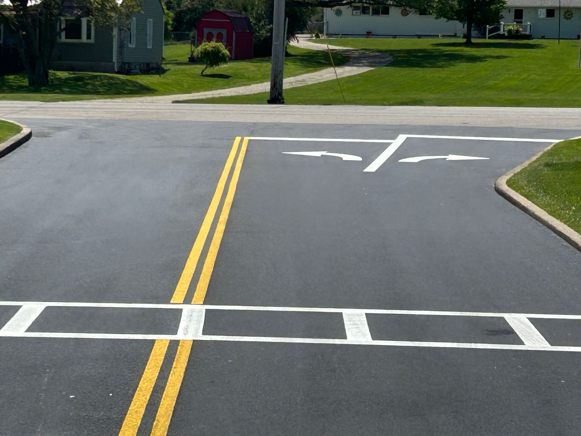 A road intersection with a white stop bar, yellow center lines, and white turn arrows painted on fresh asphalt.