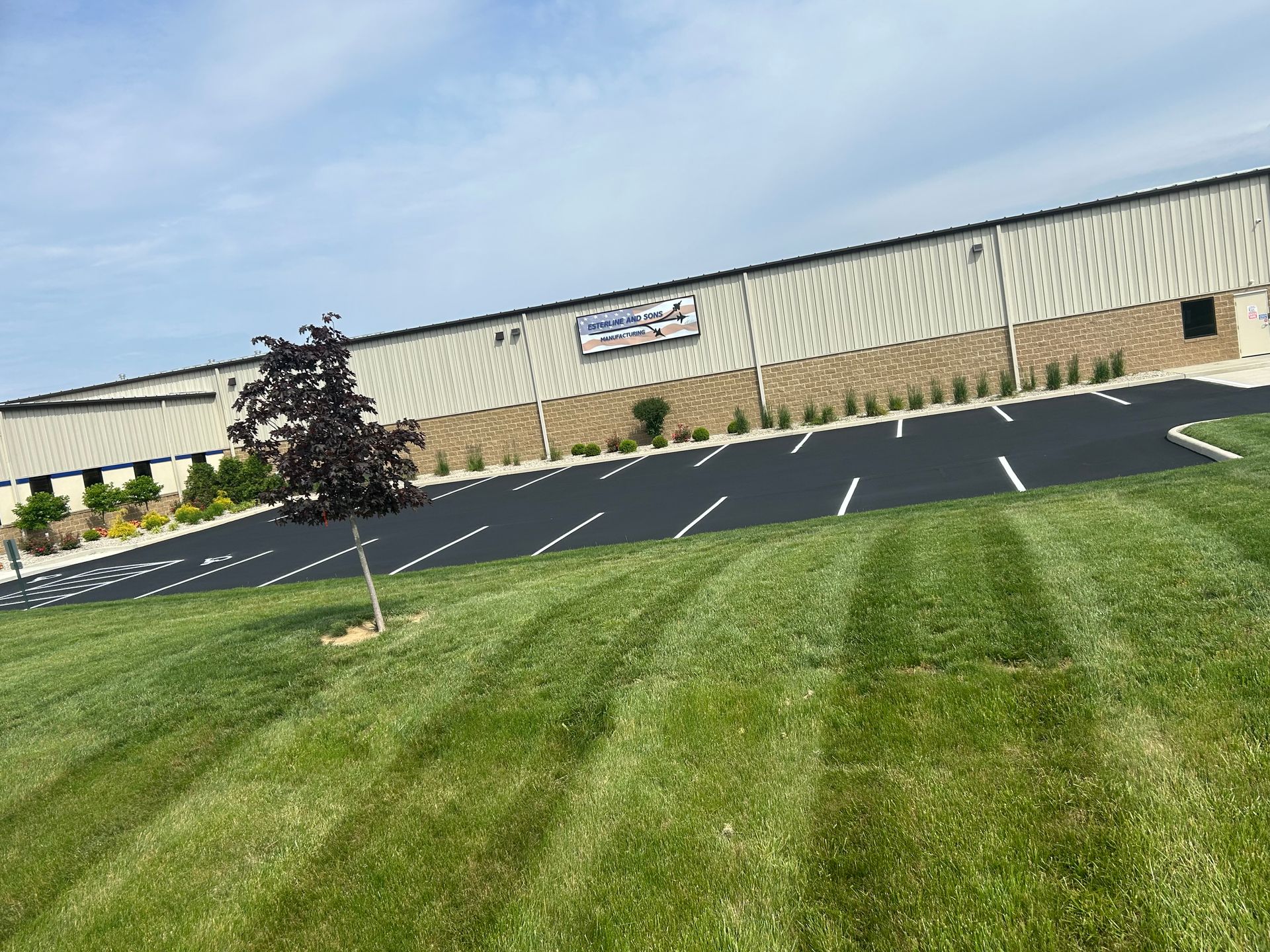 A low-angle view of a long, industrial warehouse building with a paved parking lot and a freshly mowed lawn in the foreground.