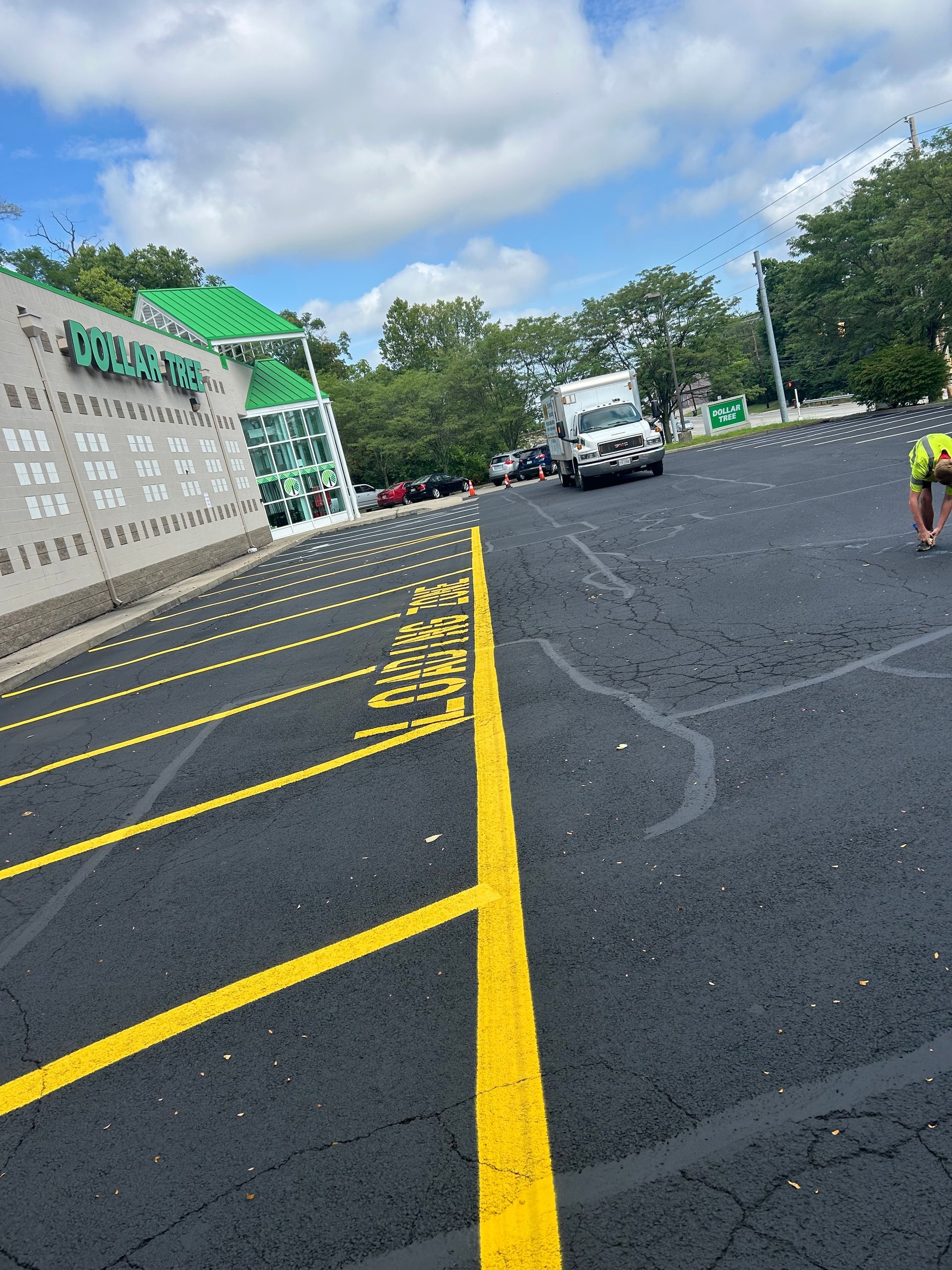 A parked delivery truck near a Dollar Tree storefront with marked parking spaces in the foreground under a cloudy sky.