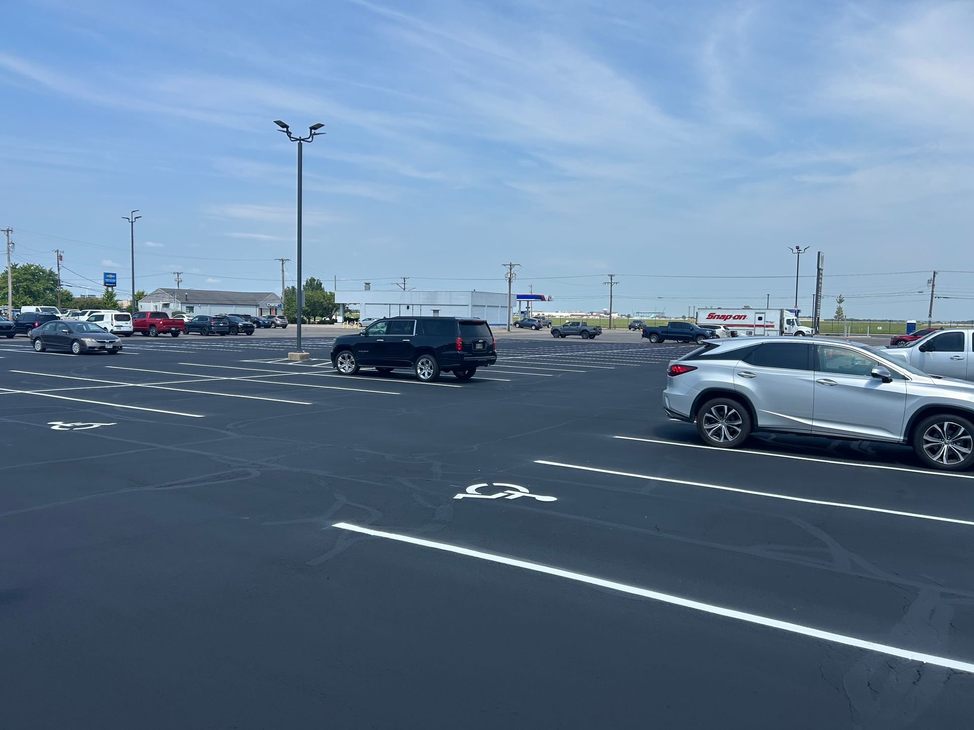 A parking lot with painted handicap symbols on the asphalt and several parked vehicles under a blue sky.