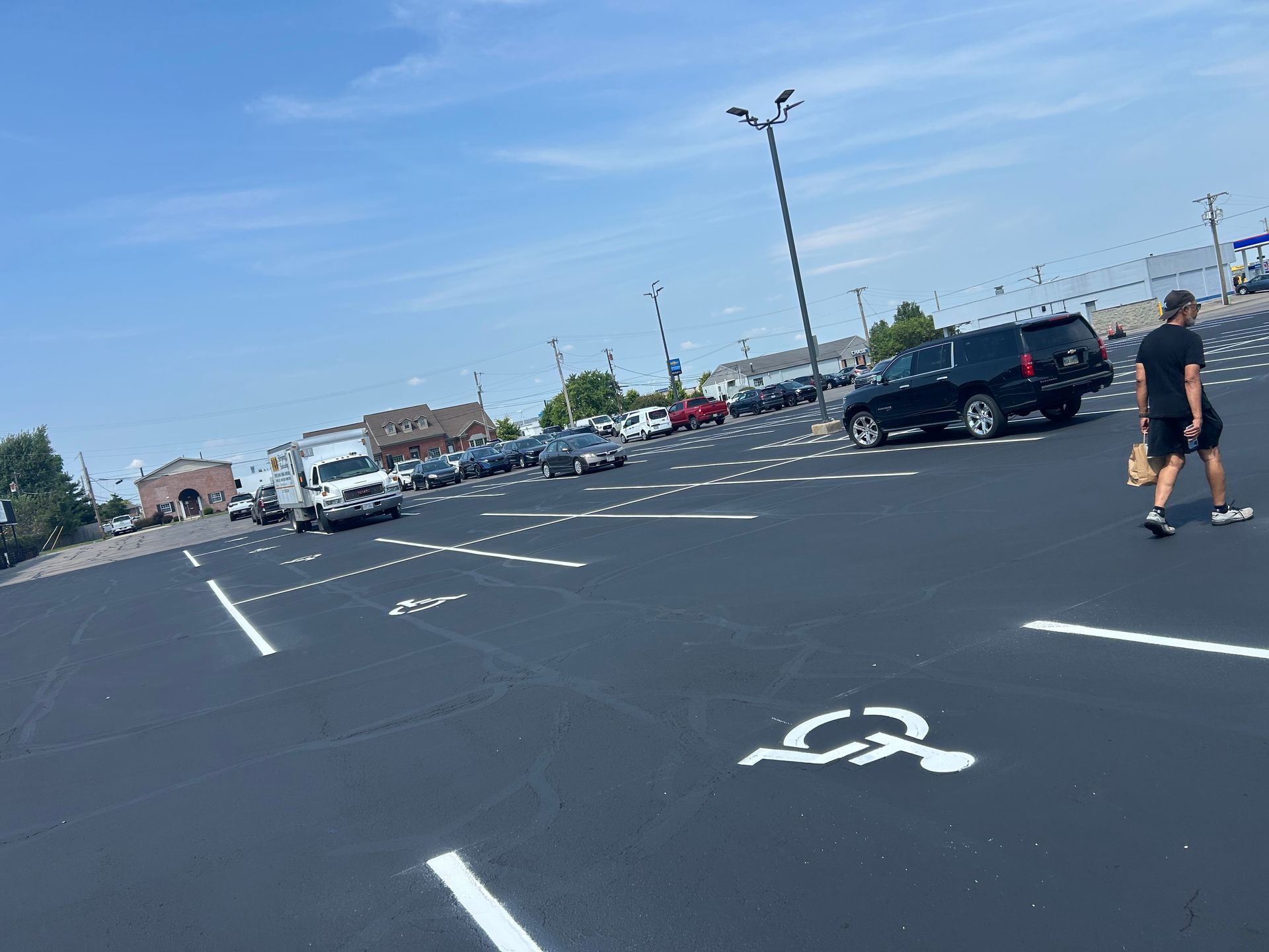 A person walks through a parking lot with painted handicap symbols on the black asphalt under a sunny sky.