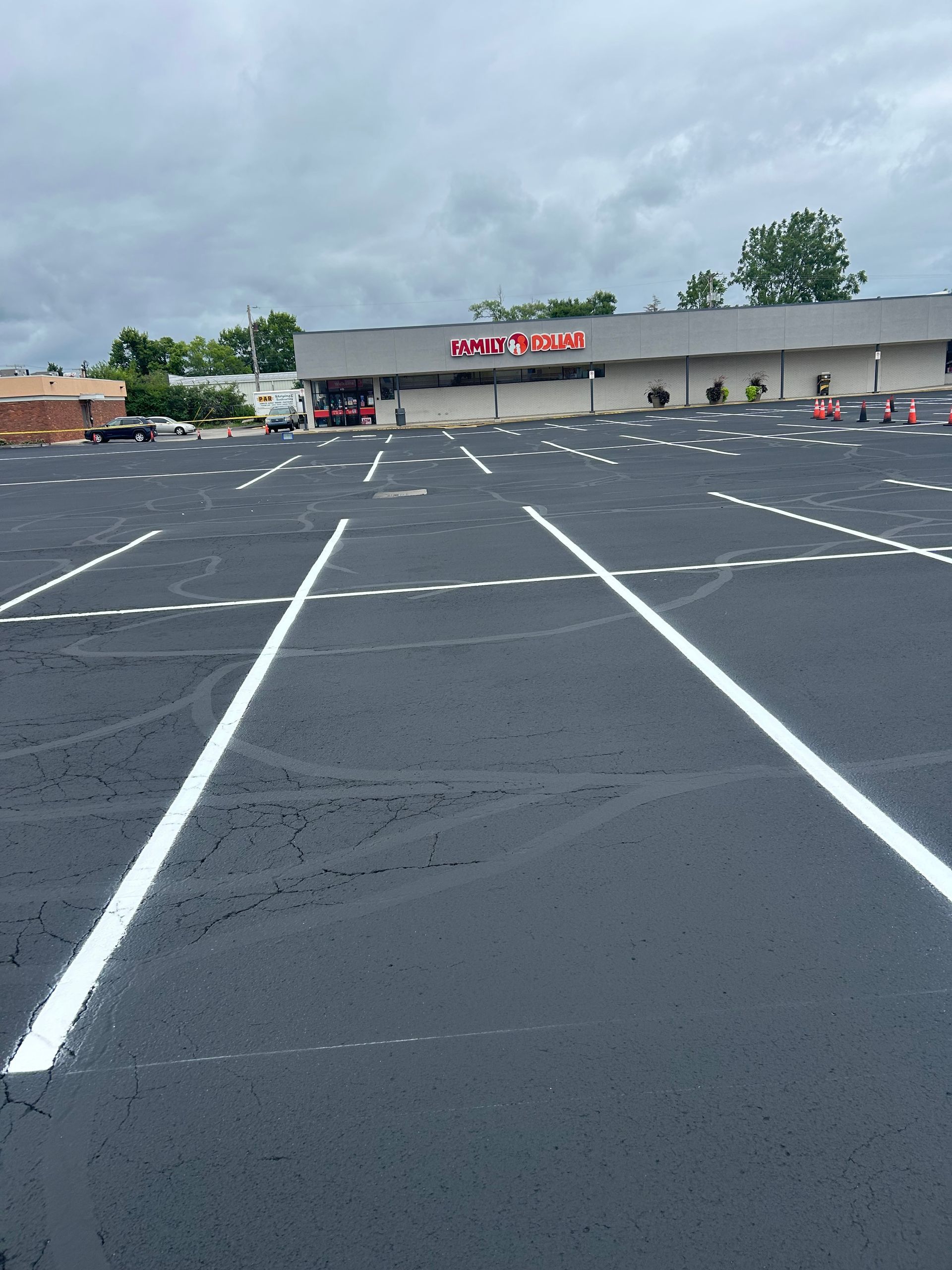 A freshly paved, empty parking lot with bright white painted lines leading toward a Dollar General store under a gray sky.