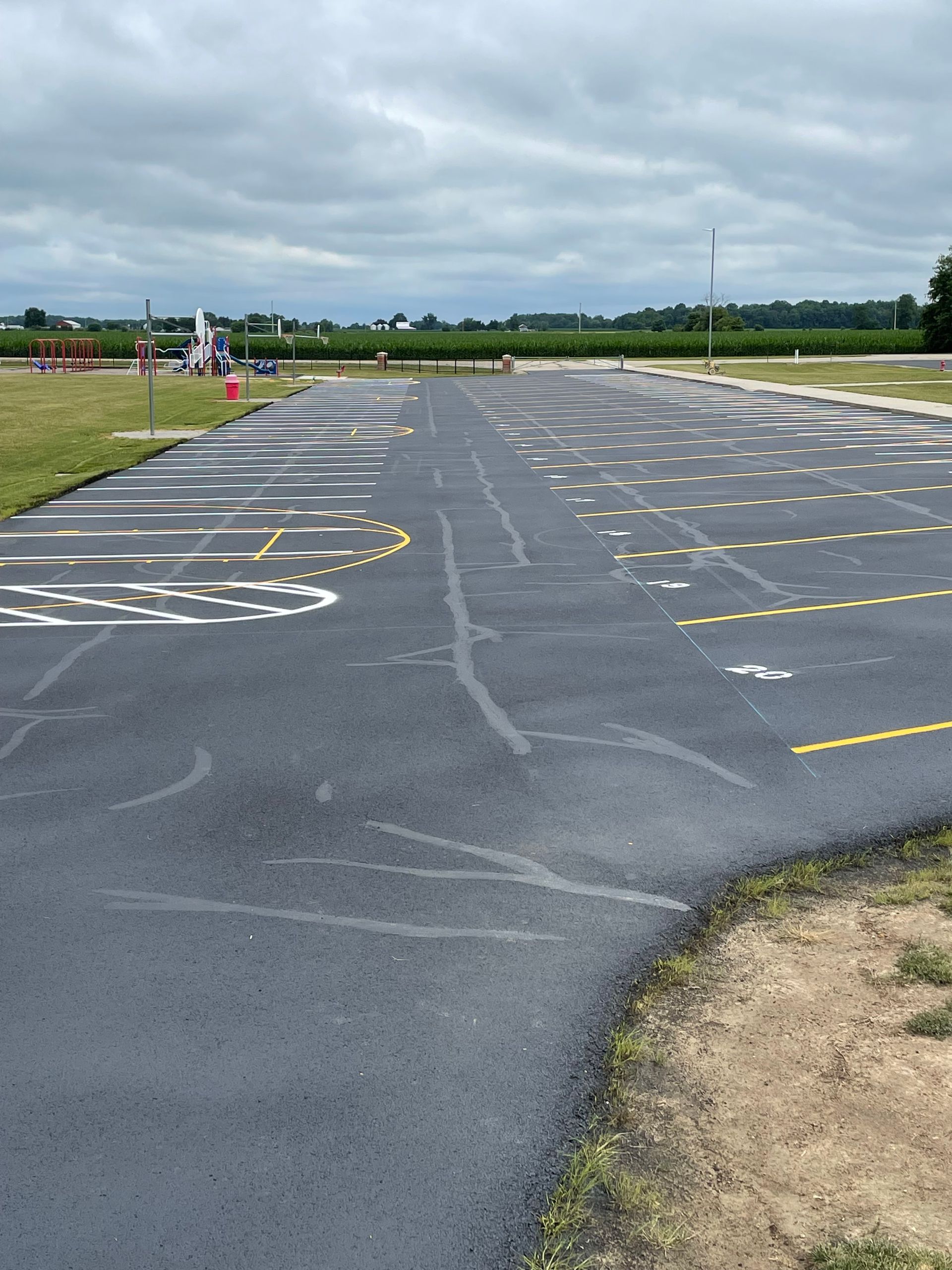 A newly paved parking lot with freshly painted white and yellow parking space markings under a cloudy sky.