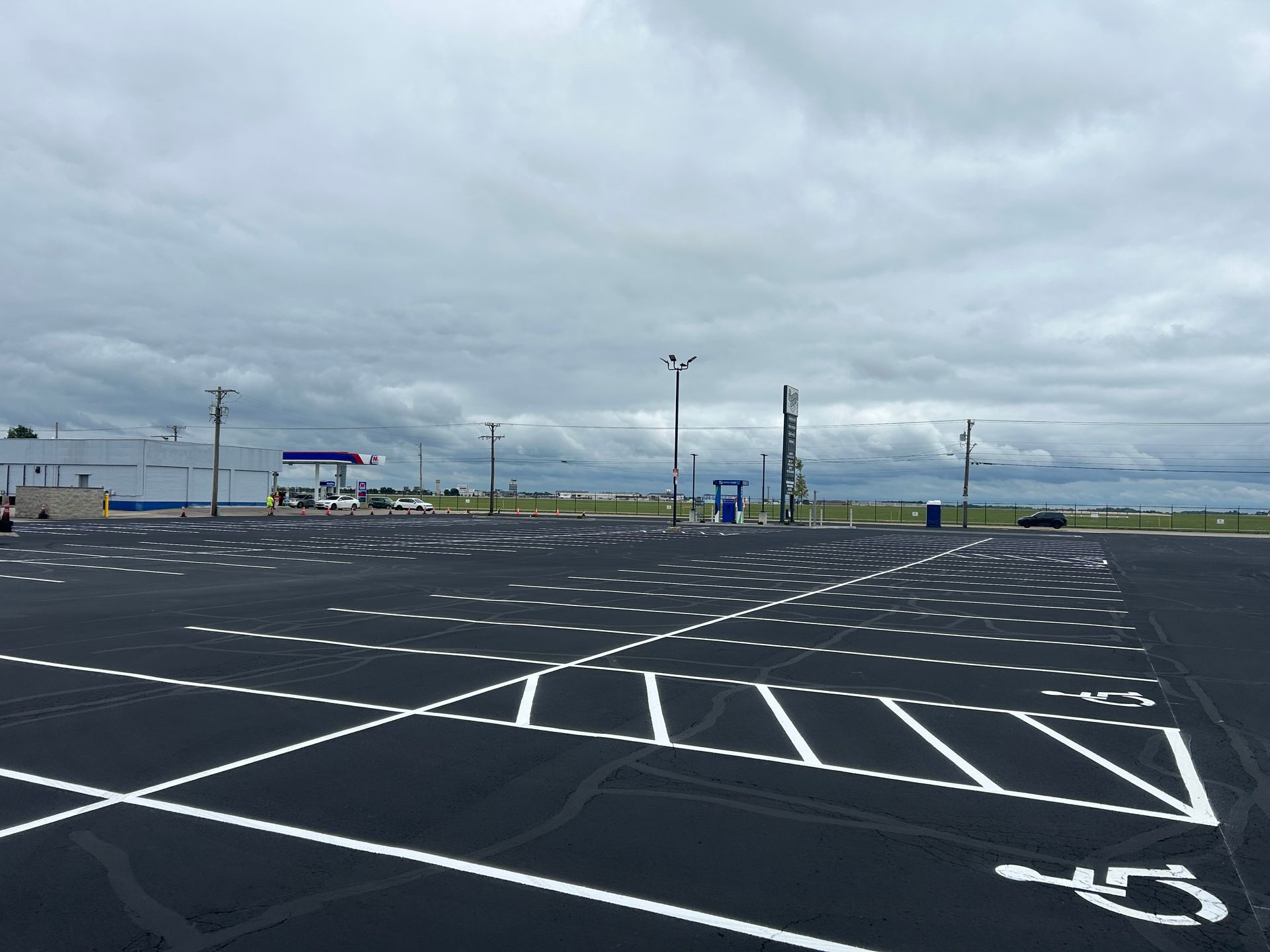 A freshly paved asphalt parking lot under a cloudy sky, featuring white painted parking lines and accessible spaces.