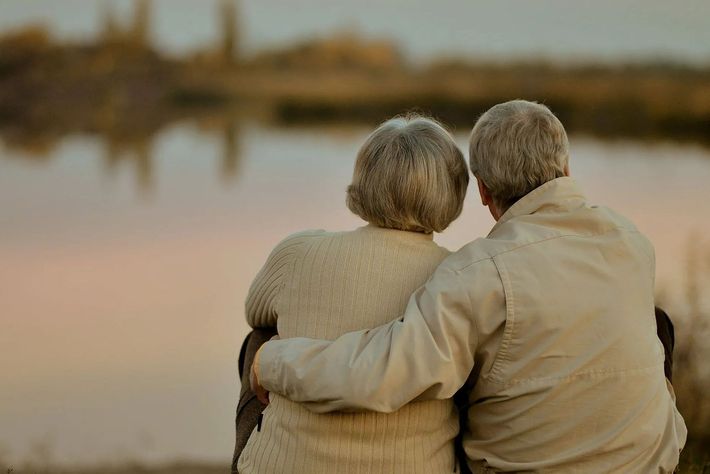 An elderly couple is sitting next to each other looking at a lake.